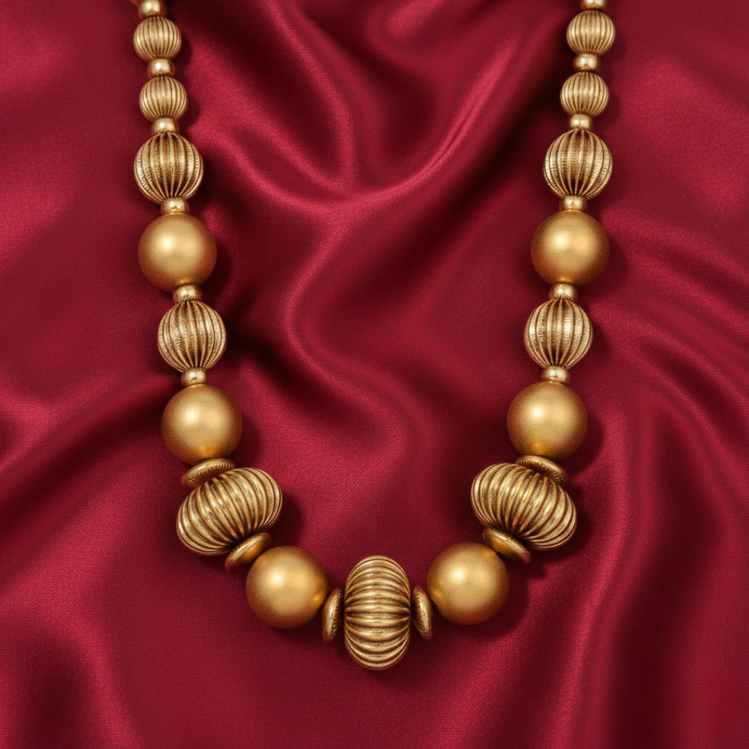 Gold tone beaded necklace on a red satin background