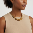 Woman wearing a gold tone beaded necklace against a neutral background