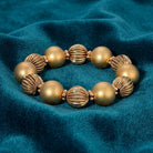 Gold colored beaded bracelet resting on teal fabric 