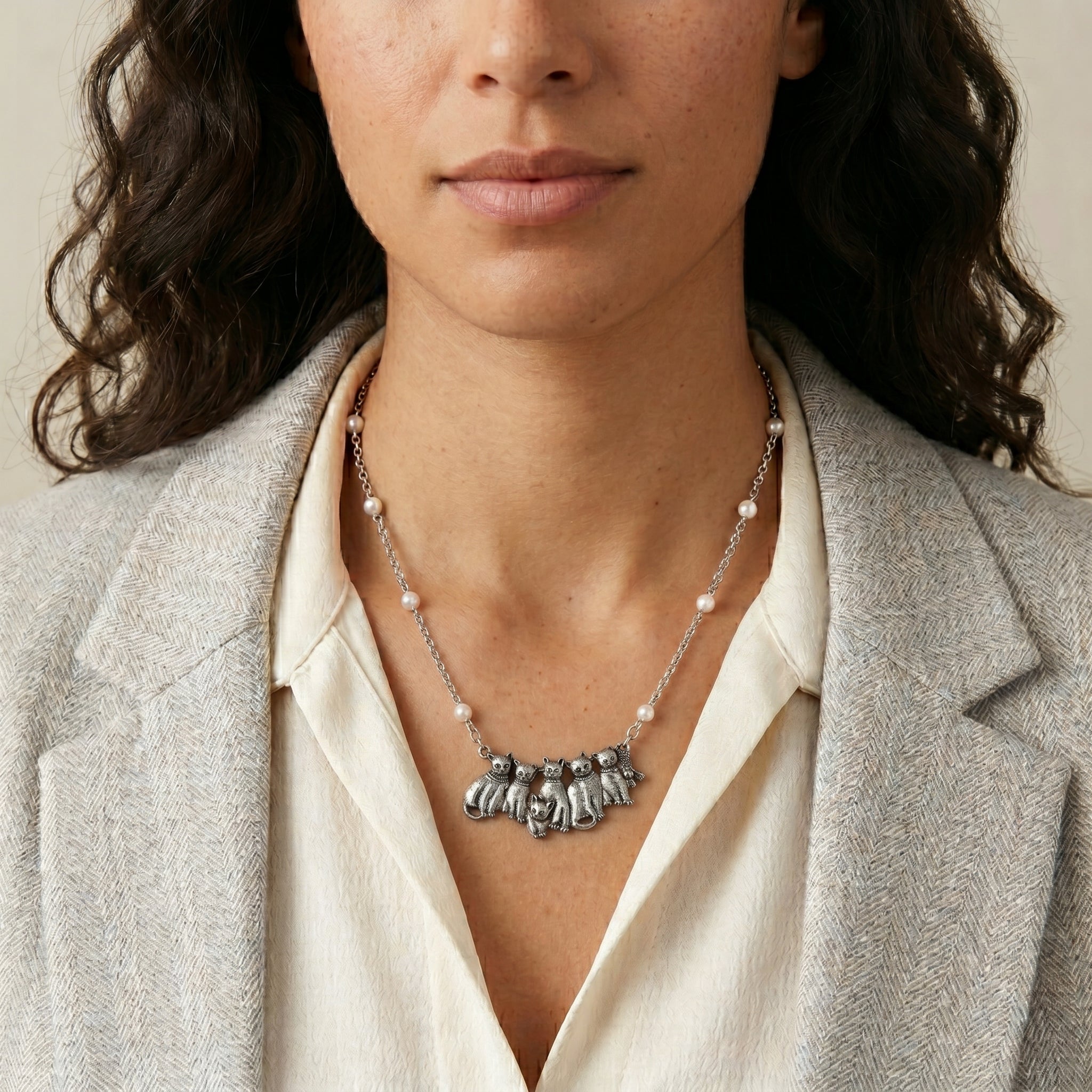 Six antiqued silver tone cats on a necklace with white faux pearl accents worn by a woman in a blazer
