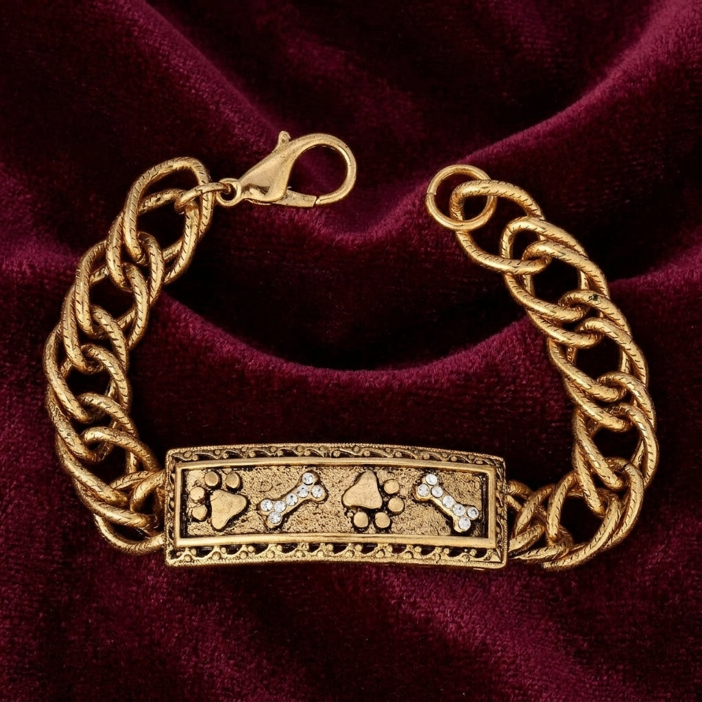 Gold tone bracelet with pet paws and bones motif and crystal accents on a red satin fabric surface