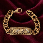 Gold tone bracelet with pet paws and bones motif and crystal accents on a red satin fabric surface