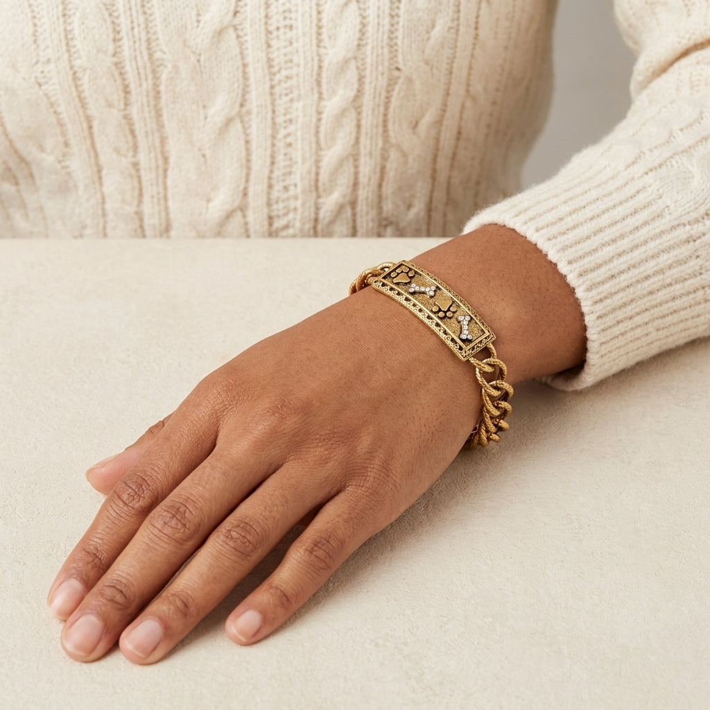 Gold tone pet paws and bones motif with crystal accents worn by a woman on her wrist as she wears a cream sweater