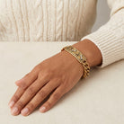 Gold tone pet paws and bones motif with crystal accents worn by a woman on her wrist as she wears a cream sweater