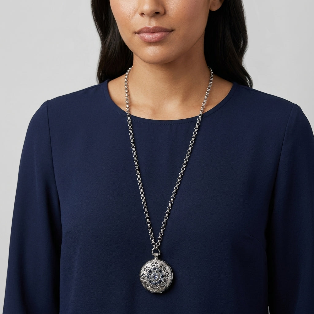 Woman in a blue top wearing a silver tone pocket watch style locket that has light blue sapphire crystal accents