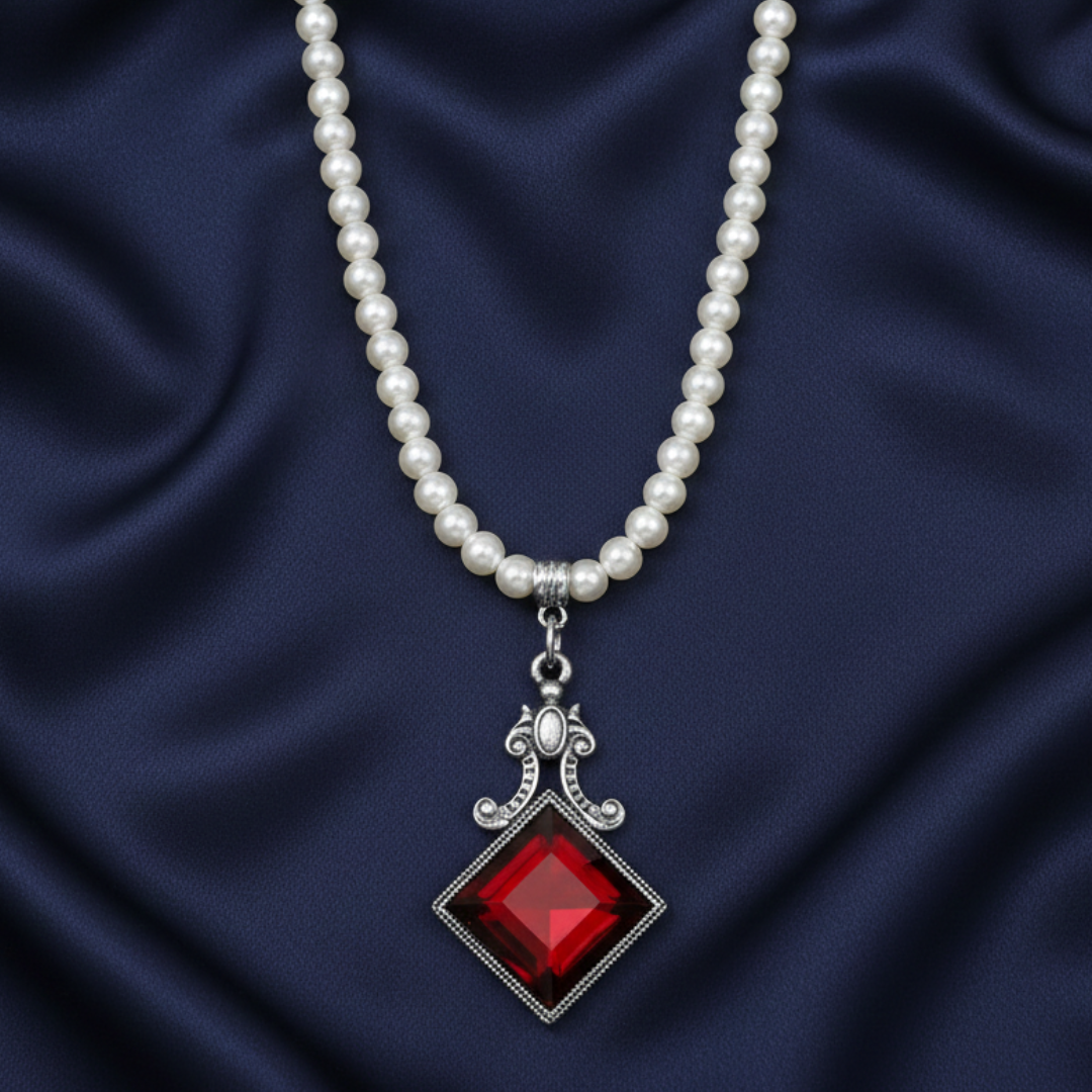 Faux pearl necklace with a large diamond-shaped red crystal pendant on a dark blue fabric background