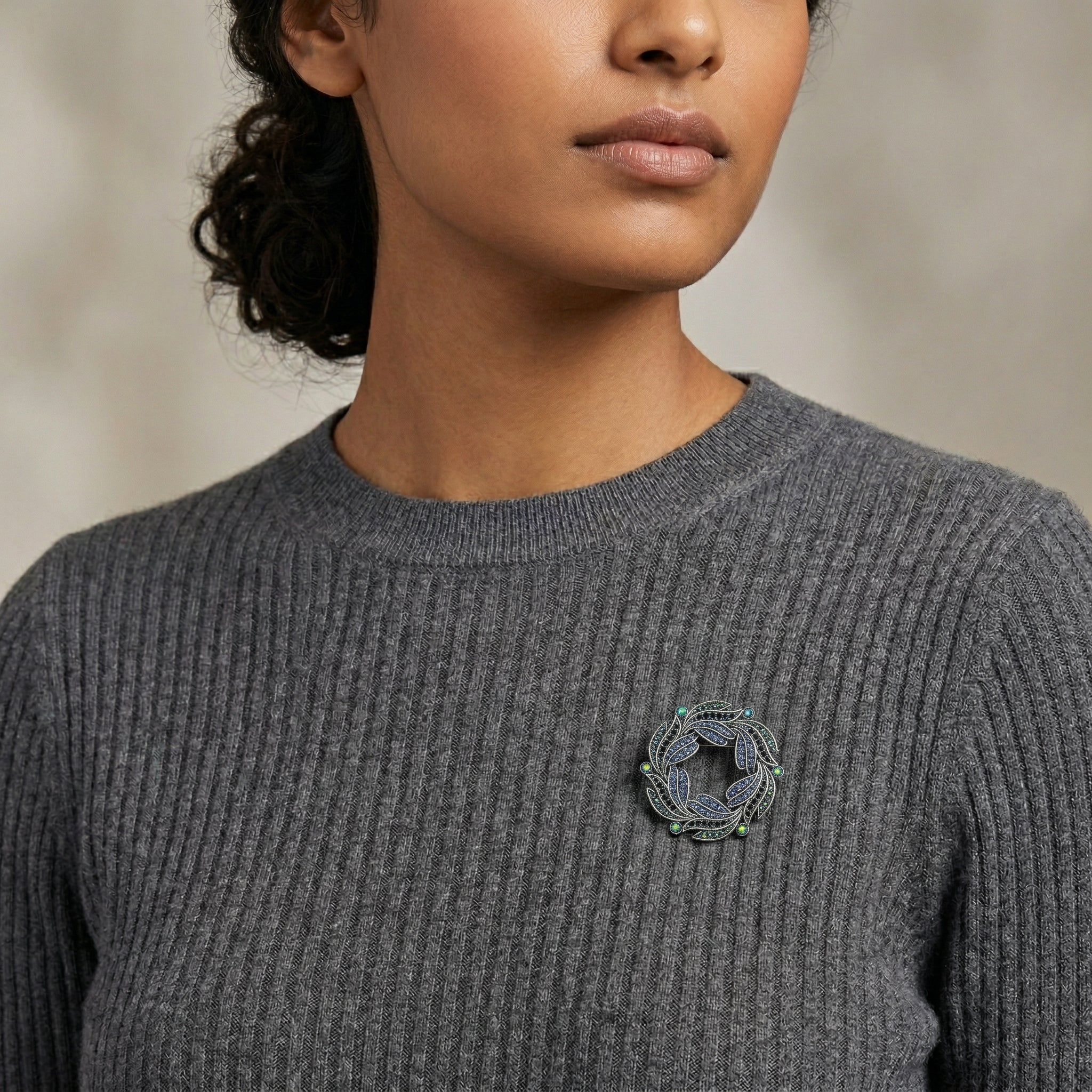 Person wearing a gray sweater with a decorative AB crystal brooch on a neutral background