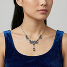 Woman wearing a detailed AB crystal necklace with a blue top against a neutral background
