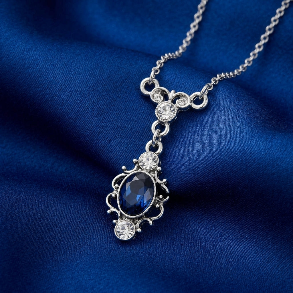 Silver necklace with a blue teardrop crystal pendant on a blue fabric background