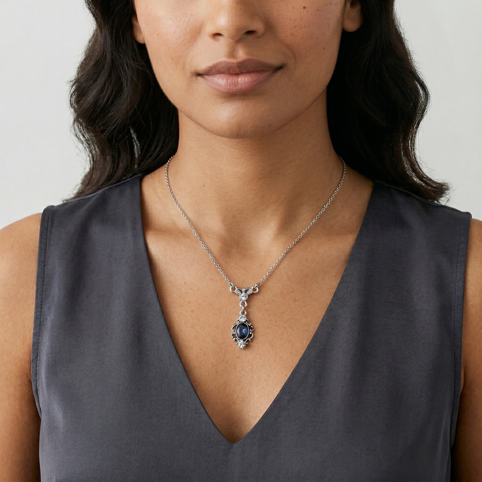 Woman wearing a silver necklace with a blue teardrop crystal pendant against a neutral background