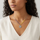 Woman wearing a necklace with colorful blue and yellow beads and a silver peace pendant