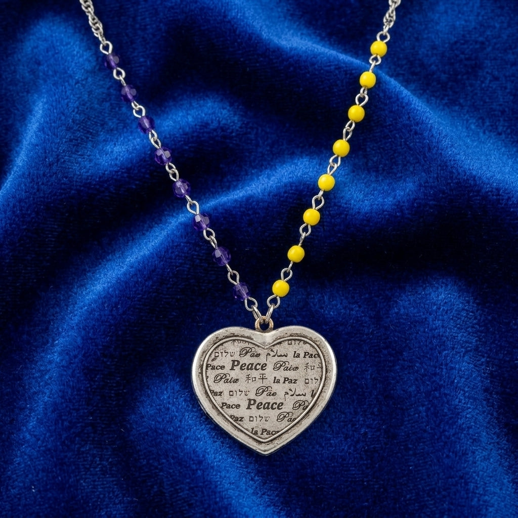Necklace with blue and yellow beads and a heart-shaped peace pendant on a blue fabric background