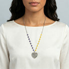 Woman wearing a necklace with blue and yellow beads and a heart-shaped peace pendant pendant on a plain background