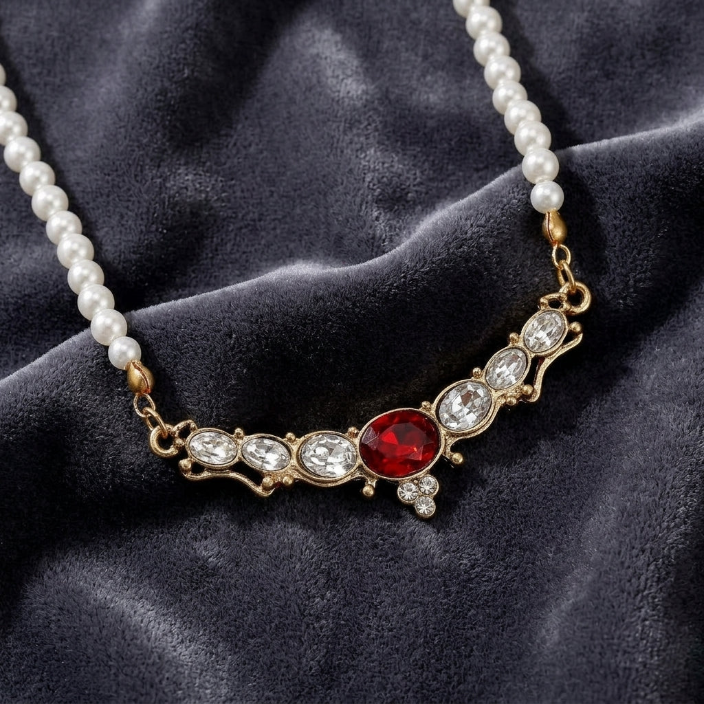 Pearl necklace with a red crystal and gold accents on a dark fabric background