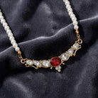 Pearl necklace with a red crystal and gold accents on a dark fabric background