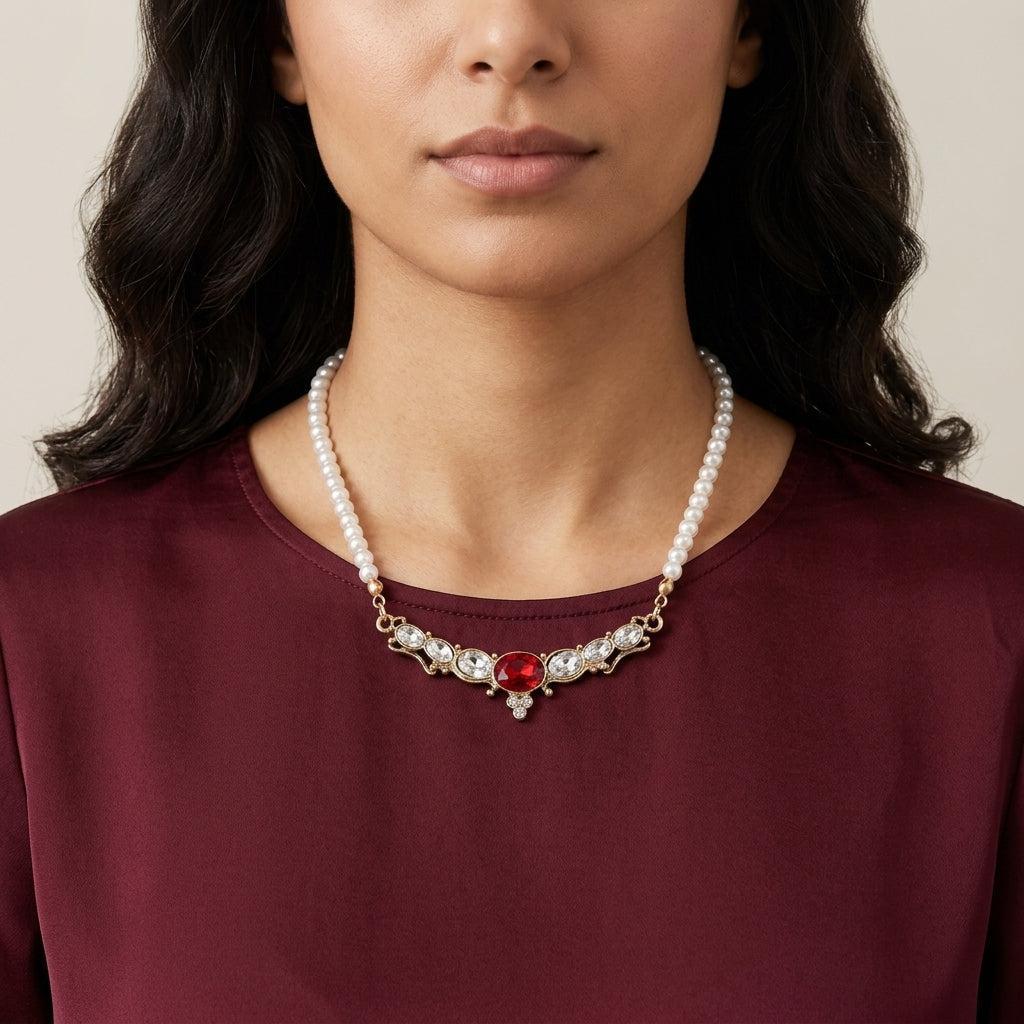 Woman wearing a pearl necklace with a red crystal on a plain background