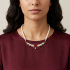 Woman wearing a pearl necklace with a red crystal on a plain background