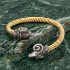 Gold bracelet with silver rams head charms on a green marble surface