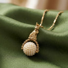 Gold tone cat pendant spinner necklace that has white faux pearls resting on green fabric surface