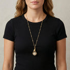 Woman wearing a black top with a gold tone cat pendant spinner necklace that has white faux pearls