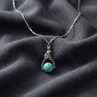 Silver tone tube chain cat and turquoise stone spinner pendant necklace resting on dark gray fabric 