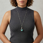 Woman in a dark gray sleeveless top wearing a silver tone tube chain cat and turquoise stone spinner pendant necklace