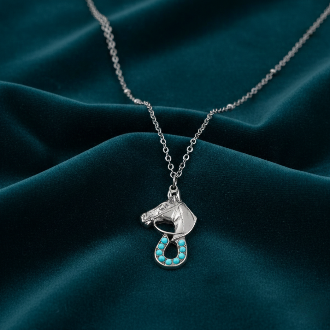 Silver horse pendant necklace with turquoise stones on a dark green fabric background