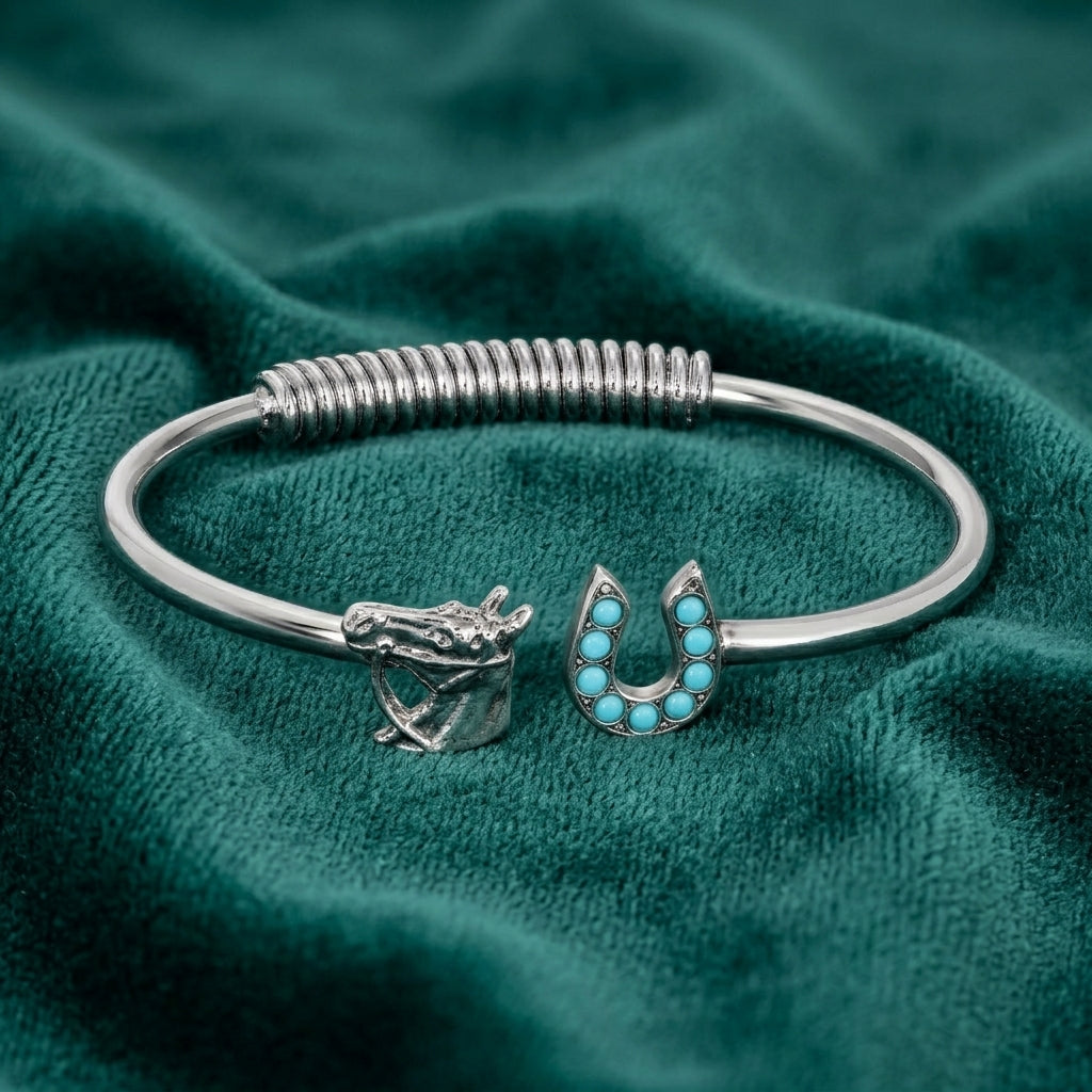 Silver bracelet with horse and horseshoe charms that have turquoise stone accents on a teal fabric background