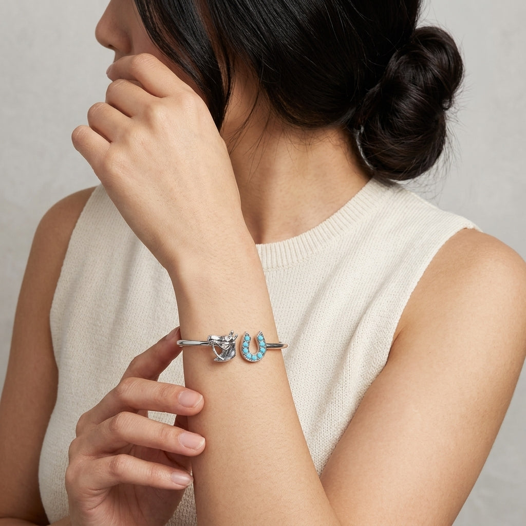 Woman wearing a silver bracelet with horse head and horseshoe designs with blue turquoise stones on a neutral background