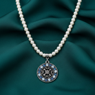 Faux pearl necklace with a decorative crystal pendant on a teal fabric background