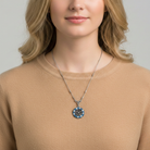 Woman wearing a necklace with a blue pendant and many crystals against a neutral background
