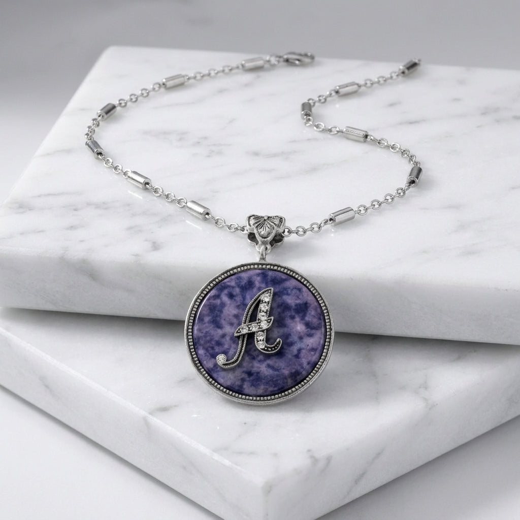Necklace with a purple sodalite pendant and letter 'A' initial on a marble surface