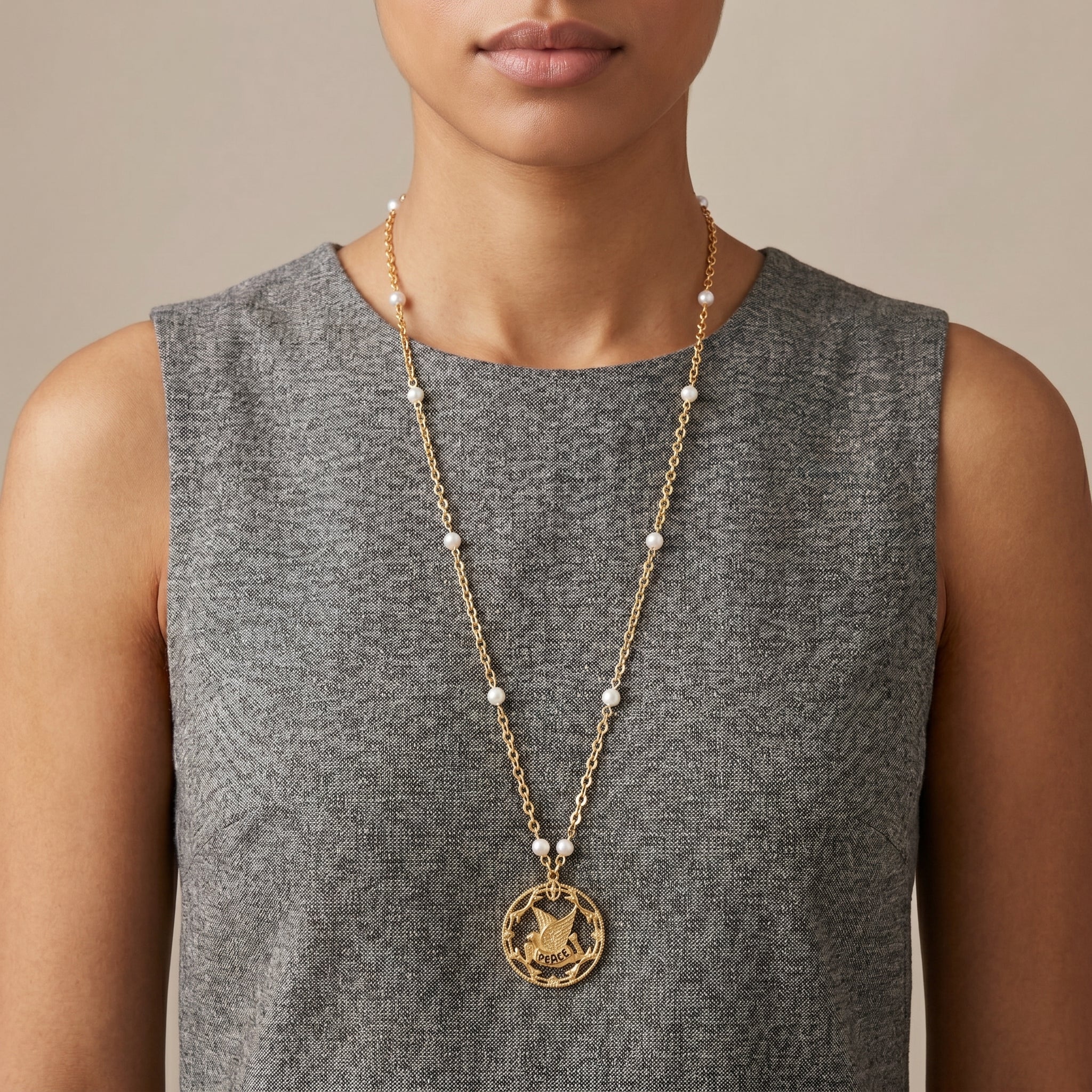 Woman in a gray top wearing a gold tone necklace with white faux pearls and a dove peace medallion pendant