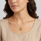 Woman wearing a gold tone peace pendant necklace with white faux pearls on the chain