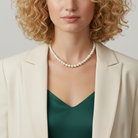 Woman wearing a faux pearl necklace with a beige blazer and green top against a neutral background