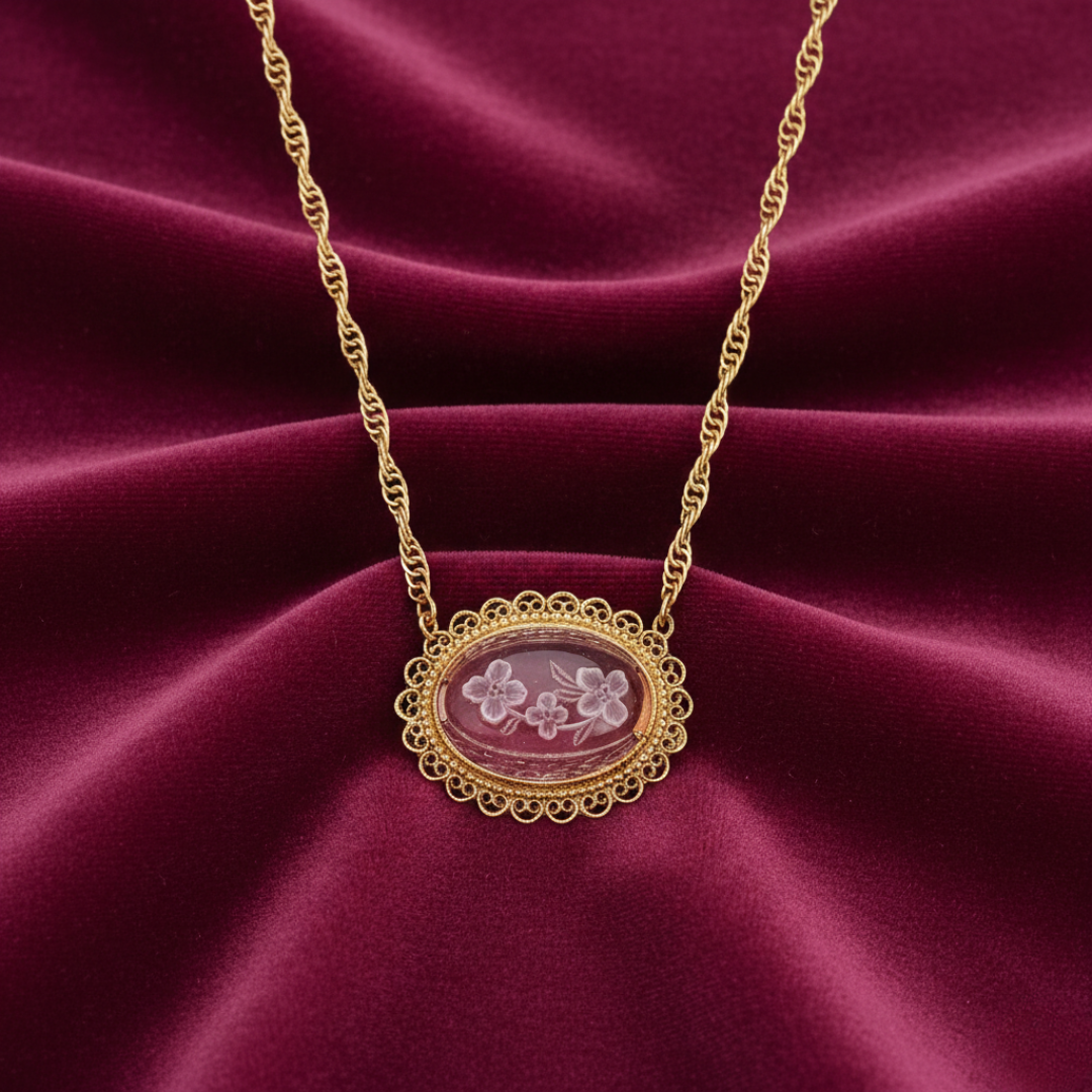 Gold necklace with a light amethyst pendant and an inner floral design set against a dark pink and red fabric background