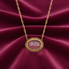 Gold necklace with a light amethyst pendant and an inner floral design set against a dark pink and red fabric background