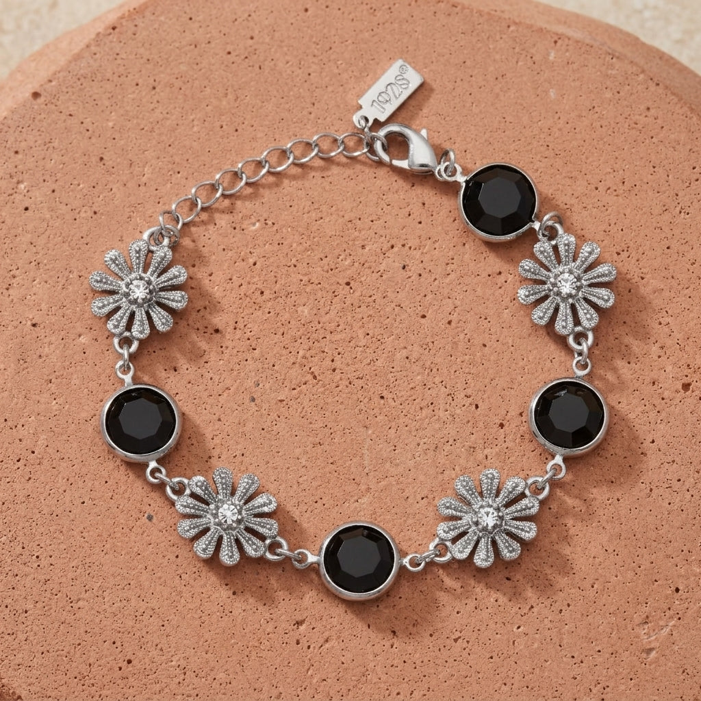 Silver bracelet with black crystals and floral designs on a soft red sandstone surface