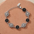 Silver bracelet with black crystals and floral designs on a soft red sandstone surface