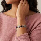 Person wearing a silver bracelet with floral designs and black crystals on a pink sweater.