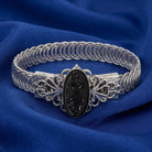 Silver bracelet with intricate design on a blue fabric background