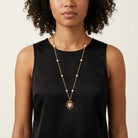 Woman wearing a gold tone chain necklace with white faux pearls and a pink heart-shaped cameo pendant 