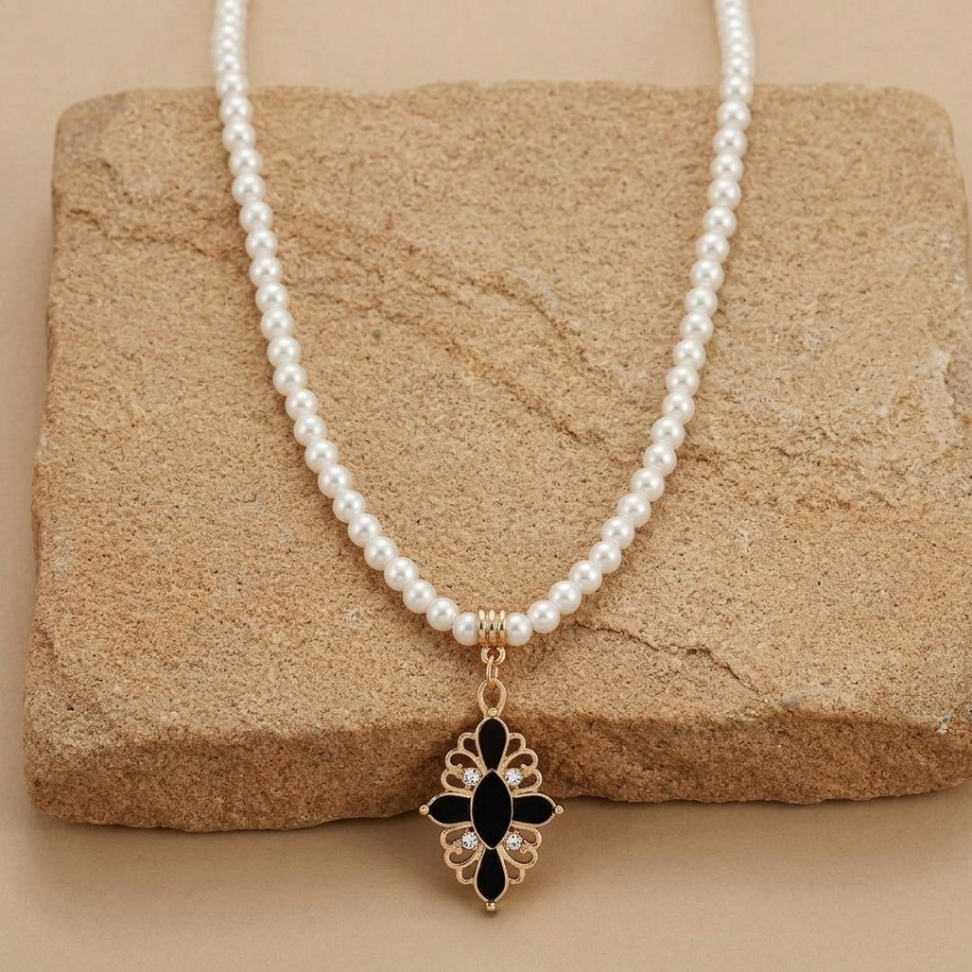 White faux pearl necklace with black stone cross pendant and crystal accents resting on light-colored sandstone