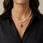 Woman in a black outfit wearing a white faux pearl necklace with a black stone cross and crystal pendant 
