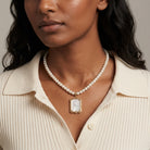Woman wearing a pearl necklace with a glass pendant and clear crystal center against a neutral background