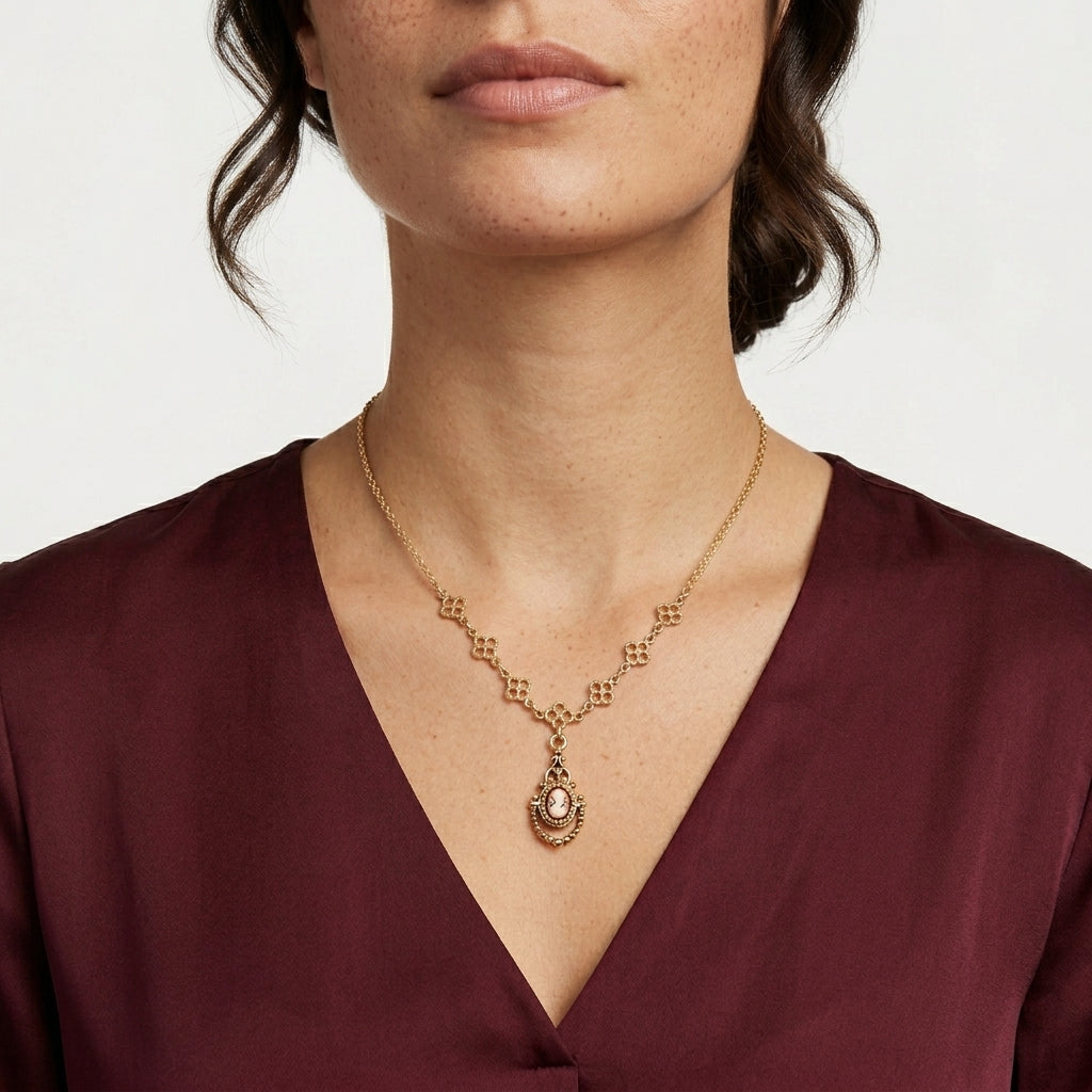 Woman wearing a gold necklace with a red cameo pendant on a plain background