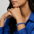 Woman wearing a blue beaded bracelet with a blue top on a gray background