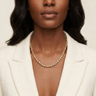 Woman wearing a gold necklace with pave clear crystals on a beige background