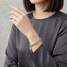 Person wearing a silver bracelet with shimmering clear crystals on a plain background