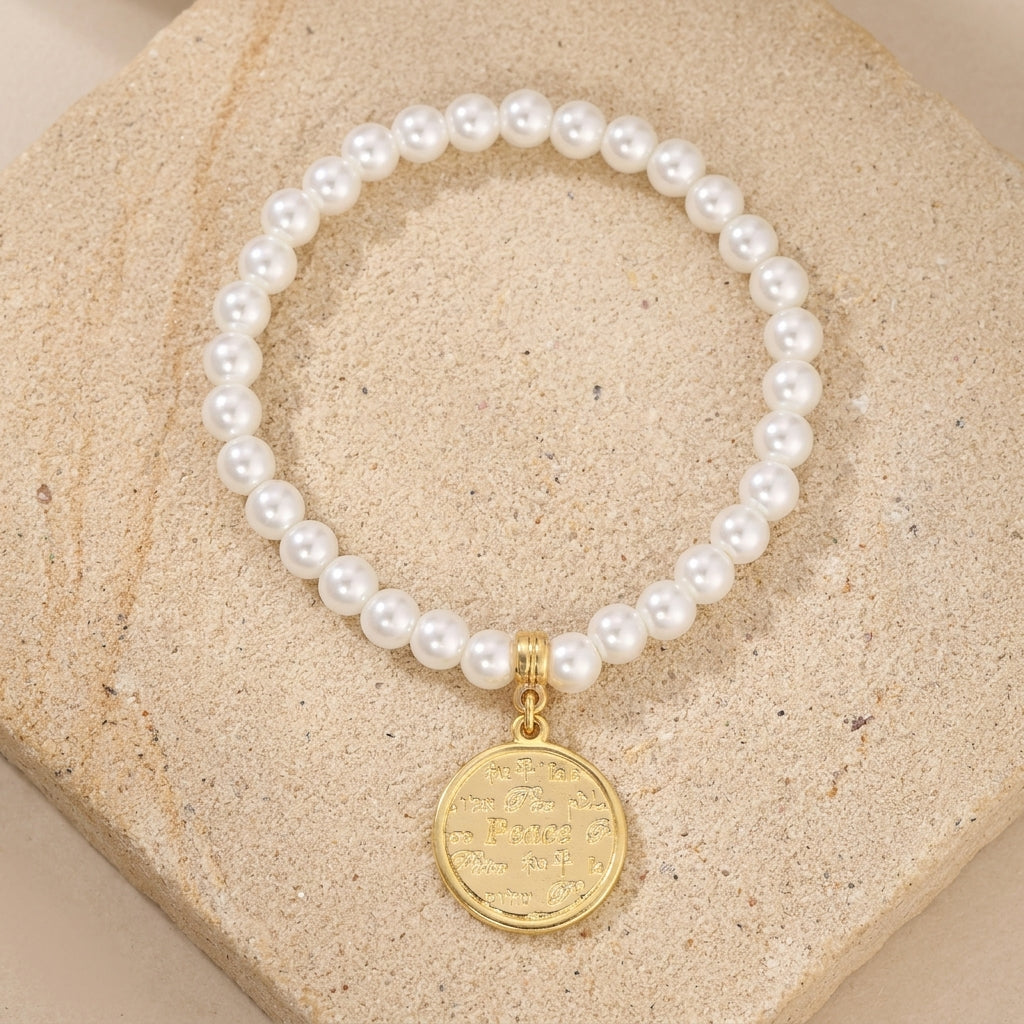 Pearl bracelet with a gold tone peace charm on a beige stone surface